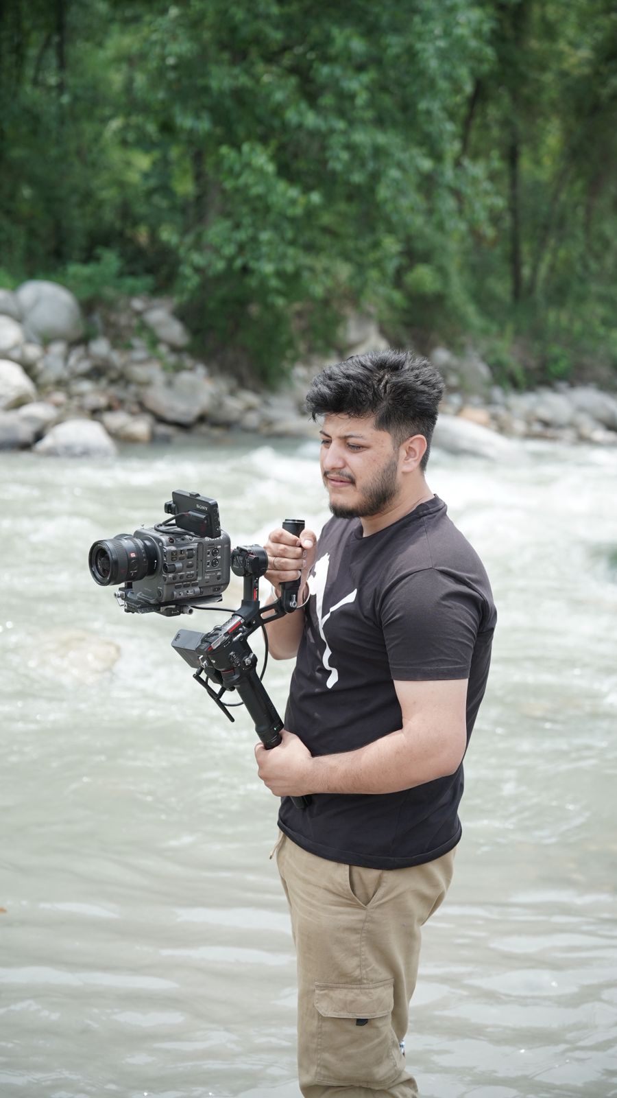 Cinematographer filming with a gimbal stabilizer beside a river during a music video shoot
