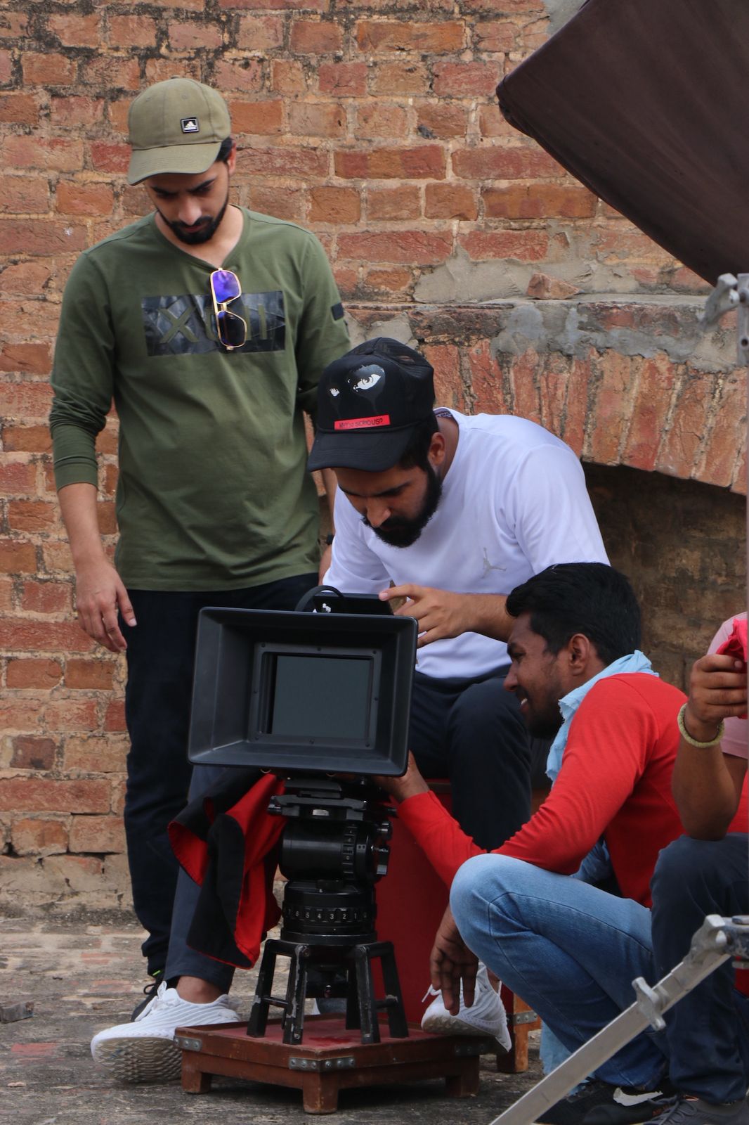Production crew operating a cinema camera on set against a brick wall backdrop